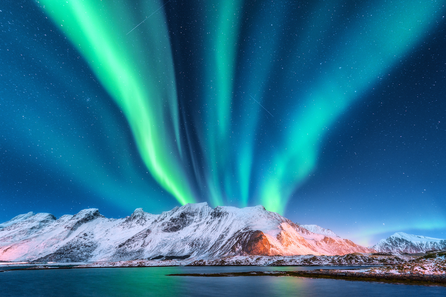 Aurora borealis. Lofoten islands, Norway. Aurora. Green northern lights. Starry sky with polar lights. Night winter landscape with aurora, sea with sky reflection and snowy mountains.Nature background